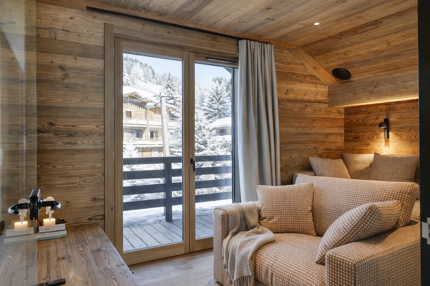 Salon cosy, canapé et baies ouvertes sur la neige